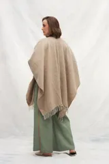 Ruana de lana 100% sin teñir en color tostado, con diseño de punto acanalado y terminación de flecos en el ruedo.
