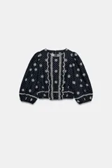 Blusa azul marino con estampado de lunares blancos, cuello redondo y mangas abullonadas. Presenta detalles de bordados perforados, volantes delanteros y acabados elásticos.