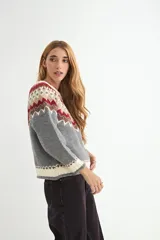 Buzo de punto con diseño de jacquard en el canesú, cuello redondo y mangas largas. Presenta un patrón geométrico multicolor en tonos crema, mostaza, bordó y azul marino sobre una base crema.