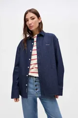 Camisa de denim azul oscuro con cuello clásico, cierre frontal de botones y bordado de marca en el pecho.