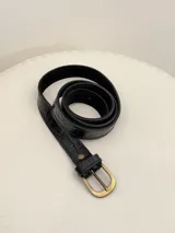 Cinto de cuero negro con textura efecto cocodrilo y hebilla metálica en tono bronce.