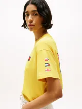 Remera amarilla de algodón con corte amplio, cuello redondo y hombros caídos. Presenta un logo pequeño de Tommy Hilfiger en el pecho, un logo en la manga y un logo grande en la espalda. Pertenece a la colección Hilfiger Sailing.
