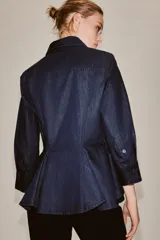 Camisa de denim azul oscuro con cuello solapa, manga larga con puños y diseño peplum en el bajo. Presenta cierre frontal con botones ocultos por solapa.