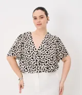 Blusa de crepé satinado con estampado de lunares, escote en V cruzado y mangas cortas tipo campana.