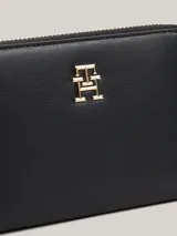 Billetera negra de poliuretano con cierre de cremallera y logo metálico dorado de Tommy Hilfiger en el frente.