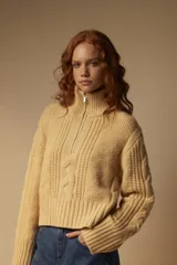 Sweater tejido color crema con cuello alto y cierre metálico frontal parcial.