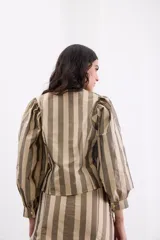 Camisa de tafeta con diseño de rayas verticales en tonos bronce y beige. Presenta escote en V, cierre frontal con botones y mangas largas abullonadas con puños ajustados. Su diseño incluye un corte asimétrico en el bajo.