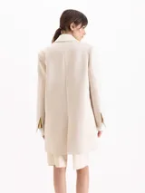 Saco sastrero estructurado confeccionado en sarga color beige, de largo por debajo de los muslos. Cuenta con cuello sastrero con solapa de pico ancha, broches dorados, hombreras, bolsillos con tapa y detalles en tela complemento en el cuello y bolsillos.
