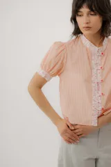 Blusa celeste a rayas blancas, de manga corta abullonada. Cuenta con cuello mao y tapeta de botones con detalles de estampado floreado en tono rosado, presentes también en el cuello y los puños.