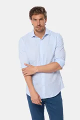 Camisa de manga larga, corte slim fit, color celeste con finas rayas verticales blancas. Presenta cuello camisero y un pequeño logo bordado en el pecho.