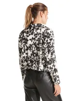 Blusa de satén con estampado floral en blanco y negro, con cuello solapa, escote en V y diseño cruzado. Presenta mangas largas con puños abotonados y ruedo con frunce elástico.