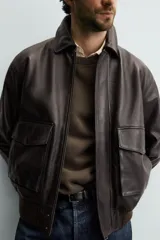 Cazadora relaxed fit de piel color marrón oscuro, con cuello solapa, manga larga y dos bolsillos plastrón con solapa en la cadera. Presenta detalle de bolsillo interior, efecto lavado y acabados en rib. El cierre frontal es con cremallera oculta por solapa con botones a presión.