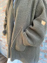 Campera de corderito color verde oliva, con cierre frontal, bolsillos laterales y etiqueta de cuero sintético en la manga.