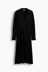 Vestido camisero midi de color negro, corte holgado con cuello, escote en V y cierre frontal de botones. Cuenta con mangas largas con puños anchos y un cinturón ajustable para anudar en la cintura.