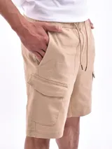 Bermuda cargo color beige, con cintura elástica y cordón ajustable. Presenta bolsillos laterales y bolsillos cargo con solapa en los costados.