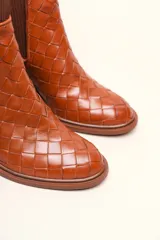 Bota tipo botineta de cuero negro con diseño trenzado artesanal en toda la capellada. Presenta paneles laterales elásticos, taco cuadrado de altura media y tirador en la parte superior trasera.