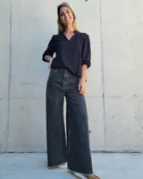 Pantalón de jean color beige, de corte recto y tiro alto, con ruedo deshilachado y cierre frontal con botón y cremallera.