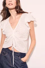 Blusa blanca de algodón con bordado broderie, escote en V con cordón ajustable, mangas cortas con volados y corte al cuerpo.