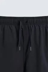 Bañador largo negro con cintura elástica ajustable mediante cordón. Presenta un panel lateral con estampado de cuadros en tonos azul y negro. Incluye bolsillos frontales y un bolsillo trasero con solapa.