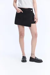 Short pollera de jean negro, con diseño cruzado asimétrico en el frente, bolsillos y tiro alto.