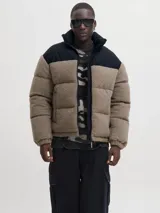 Campera puffer con diseño de bloques de color, combinando tejido teddy en tono arena y paneles negros en los hombros. Presenta cuello alto, cierre frontal y diseño acolchado.