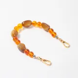 Accesorio decorativo para cartera compuesto por cuentas de resina en tonos ámbar y marrón, con ganchos metálicos dorados en los extremos.