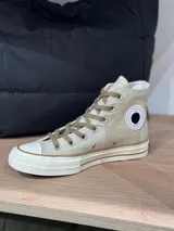 Zapatillas de lona color beige, tipo bota, con cordones marrones, puntera de goma y logo de peach engomado.