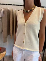 Chaleco de punto color crudo con escote en V y botones dorados.