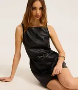 Vestido corto sin mangas de cuero sintético negro, con escote cuadrado y silueta evasé. Incluye un cinturón fino incorporado con detalle de hebilla metálica dorada.