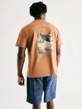Camiseta de cuello redondo y manga corta, color marrón claro, con pequeño estampado central en el pecho que incluye un ave y la leyenda 'Wings of the Seasons Hering Co'.