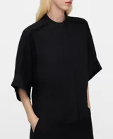 Camisa negra oversize de lino y viscosa, con cuello mao, botonadura frontal oculta por sopata, manga murciélago con vuelta bajo el codo, bolsillo en el pecho y costuras desflecadas en el canesú y las mangas.