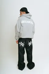 Pantalón de jean negro, corte baggy, confeccionado en denim crudo. Presenta un estampado serigrafiado en blanco con un diseño estilizado en ambos bolsillos traseros y un parche con logo en la cintura.
