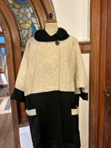 Tapado artesanal combinado en lana y paño, color marfil y negro, con cuello alto y cierre con dos botones. Tiene bolsillos en el frente.