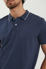 Chomba azul marino de piqué con cuello clásico y tapeta de dos botones. Detalles de ribete blanco en cuello y mangas.