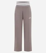 Pantalón deportivo de corte recto color marrón, confeccionado en una mezcla de modal y algodón. Presenta cintura elástica en rib con rayas blancas contrastantes, bolsillos laterales y detalle de lettering bordado en la pierna. Incluye aberturas laterales en el ruedo.