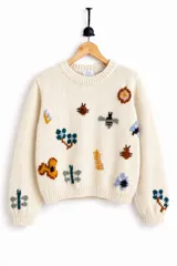 Sweater de punto jersey de lana merino en color marfil, con cuello redondo y bordados artesanales a mano de insectos y flores multicolores en el frente y las mangas.