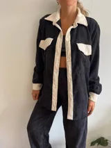 Camisa de pana negra con cuello, solapa, botones y bolsillos de parche en color crema. Corte recto y mangas largas.