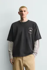 Sudadera de manga corta con corte relajado, confeccionada en algodón con interior de rizo. Presenta cuello redondo con detalle de costura en V, efecto lavado y estampado gráfico en el frente.