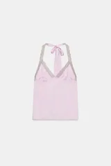 Top de satén rosado con estampado de lunares, escote en V y cuello halter con lazo para atar. Presenta detalles de encaje en contraste a lo largo del escote y los tirantes.