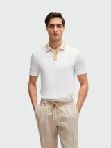 Remera polo blanca de corte slim fit, confeccionada en algodón. Presenta cuello clásico con rayas color crema y naranja, y cierre de dos botones. Marca BOSS, modelo PHILLIPSON.