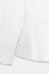 Camisa de popelín de algodón con cuello solapa, manga larga con puños y bajo con diseño peplum. Presenta cierre frontal oculto con botones.