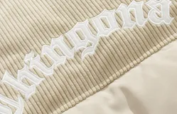 Campera puffer marrón con paneles horizontales acolchados. La parte superior de la espalda es de pana marrón con el texto 'Chingona' bordado en blanco. Posee cordón ajustable en el ruedo y se lleva superpuesta a una sudadera con capucha gris.