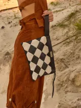 Cartera tipo sobre con diseño de ajedrez en rombos de cuero blanco y negro. Cuenta con una correa de mano integrada y detalle de placa metálica con logo.