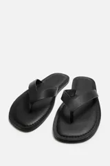 Sandalia minimalista de cuero negro, con tira delgada en el empeine y suela plana.