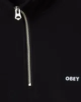 Buzo de cuello alto con cierre frontal parcial, marca Obey. Presenta diseño minimalista en color negro con logo de la marca bordado en el pecho y puños acanalados.