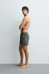 Bañador de hombre de largo medio, color celeste claro con rayas blancas horizontales. Presenta cintura elástica ajustable con cordón, bolsillos frontales y bolsillos traseros de plastrón. Incluye forro interior.