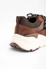Zapatilla urbana de diseño chunky, combinando paneles de gamuza y cuero en tonos chocolate con malla técnica. Presenta cordones bicolores y una suela de plataforma de goma en color crema.