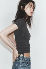 Camiseta corta de cuello redondo y manga corta, color gris oscuro, con frunces laterales ajustables mediante cordones.