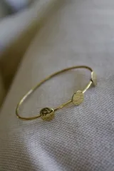 Pulsera rígida dorada con tres apliques circulares con textura martillada.