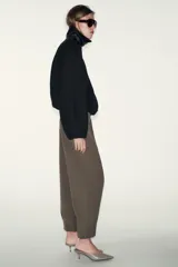 Pantalón de tiro medio con pinzas delanteras, bolsillos laterales y falsos bolsillos de vivo en la parte trasera. Presenta un corte holgado que se estrecha hacia el tobillo, con bajo acabado en pliegues y cierre frontal con cremallera, botón interior y gancho.